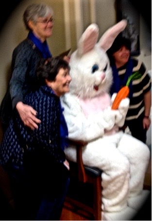 Somebody in a bunny costume, seated, with one woman on either side, standing