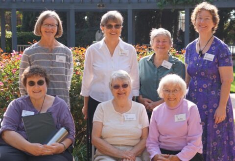 group of 7 women outdoors; 4 standing and 3 sitting in front of them