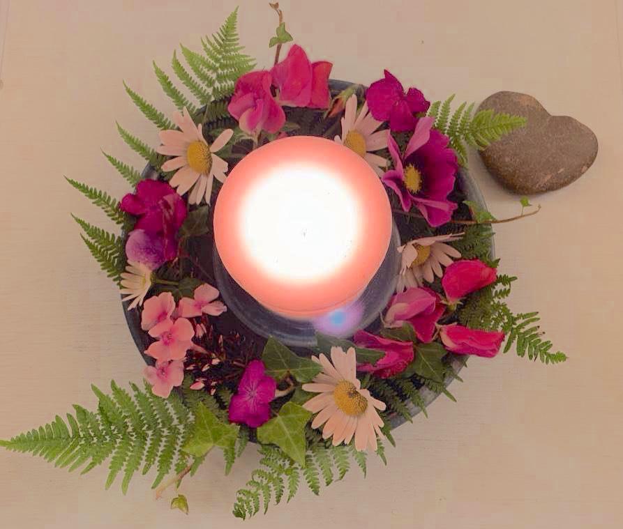 photo of light surrounded by small wreath of flowers and greenery; heart-shaped stone in upper right