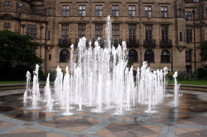 Fountain spouts arising from tiled ground in front of a tan stone building
