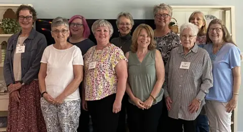 Group of smiling white women, older and middle-aged. They are wearing summer clothes.