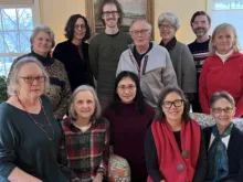 12 smiling men and women of various races, wearing winter clothes, in a living room