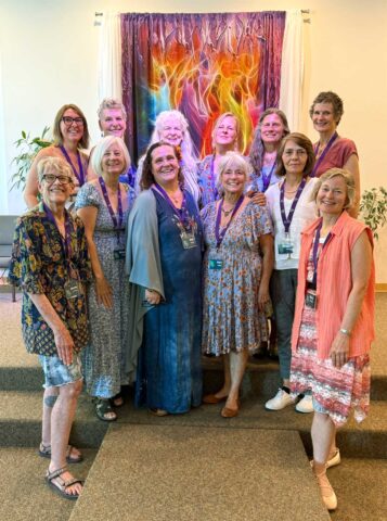 12 women standing in front of a colorful wall hanging